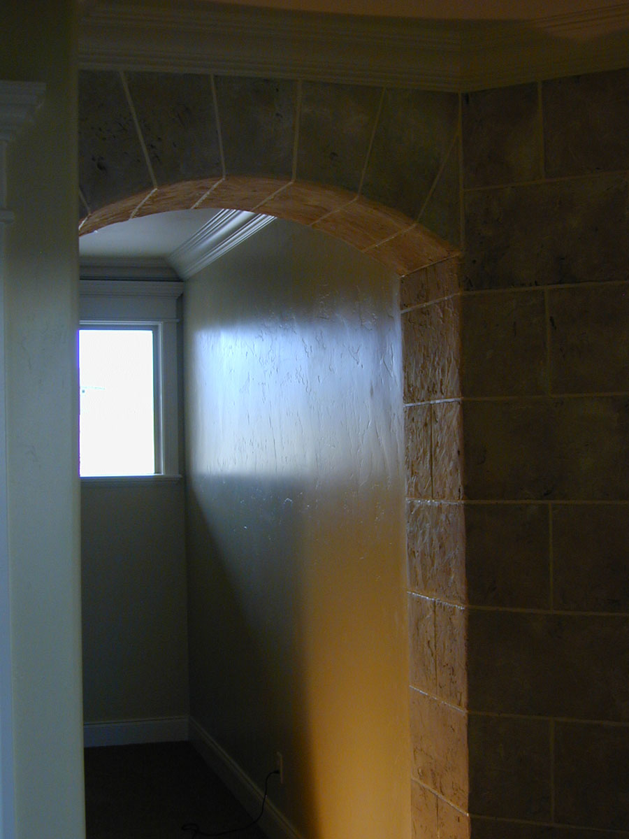 Stonework wrapped around the wall behind the fireplace, lining part of a hall.